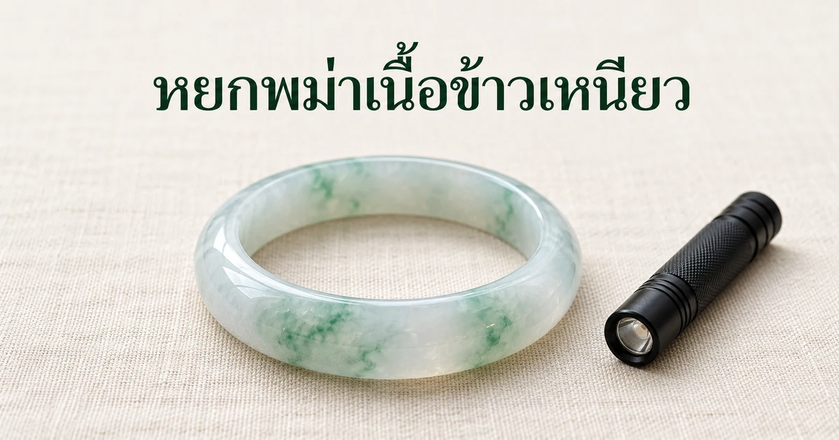 กำไลหยกพม่าข้าวเหนียวน้ำแข็งเนื้อนุ่มโปร่งแสง มีลายดอกลอยสีเขียวอ่อน วางบนผ้าลินินสีงาช้างในแสงธรรมชาตินุ่มๆ ข้างไฟฉายเล็ก