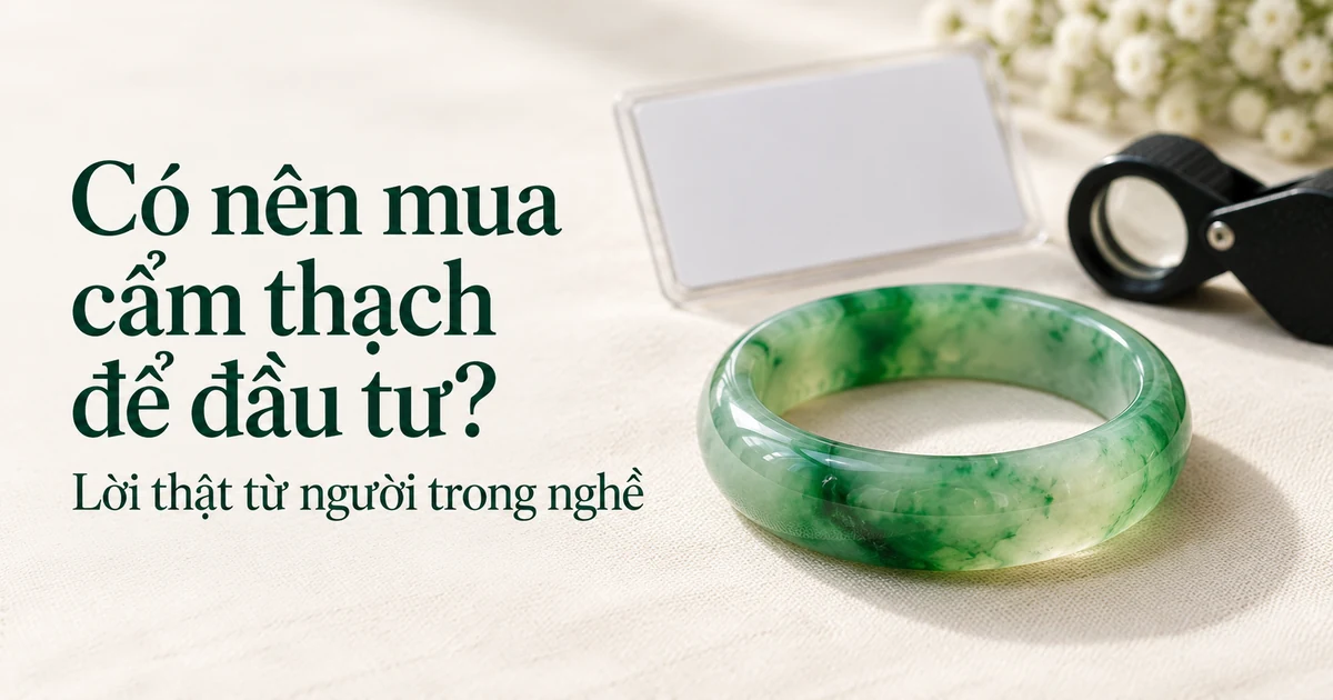 Một chiếc vòng cẩm thạch xanh trong đặt rõ nét phía trước trên vải lanh màu ngà, phía sau là tấm giấy kiểm định để trống và kính lúp kim hoàn chụp mờ, ánh sáng ban ngày dịu