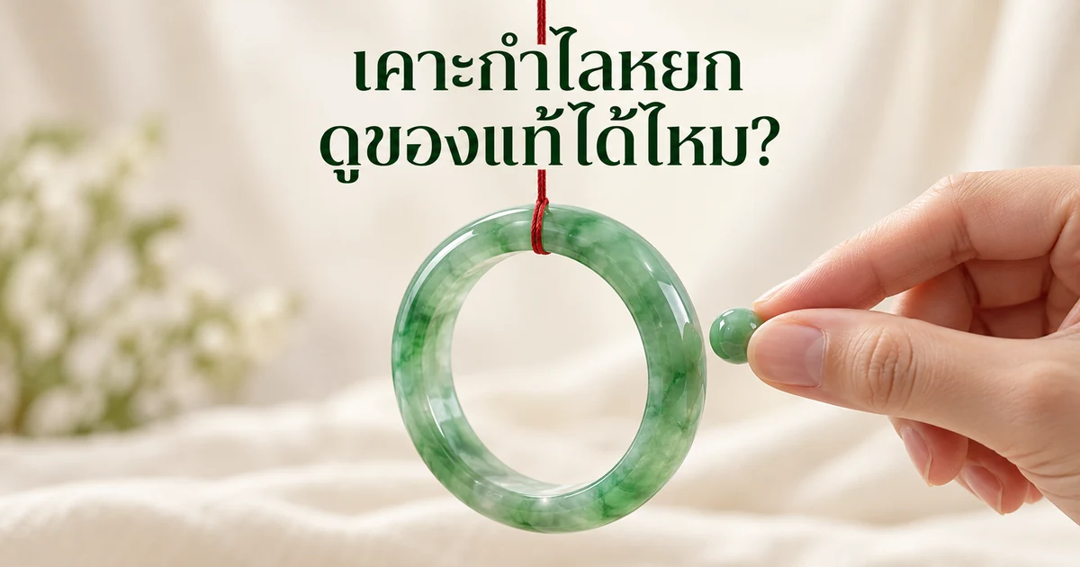 กำไลหยกพม่าสีเขียวโปร่งแสงแขวนด้วยด้ายแดงเส้นเล็ก มีลูกปัดหยกเม็ดเล็กจ่ออยู่ใกล้ขอบกำไล บนพื้นหลังสีงาช้างนุ่มๆ