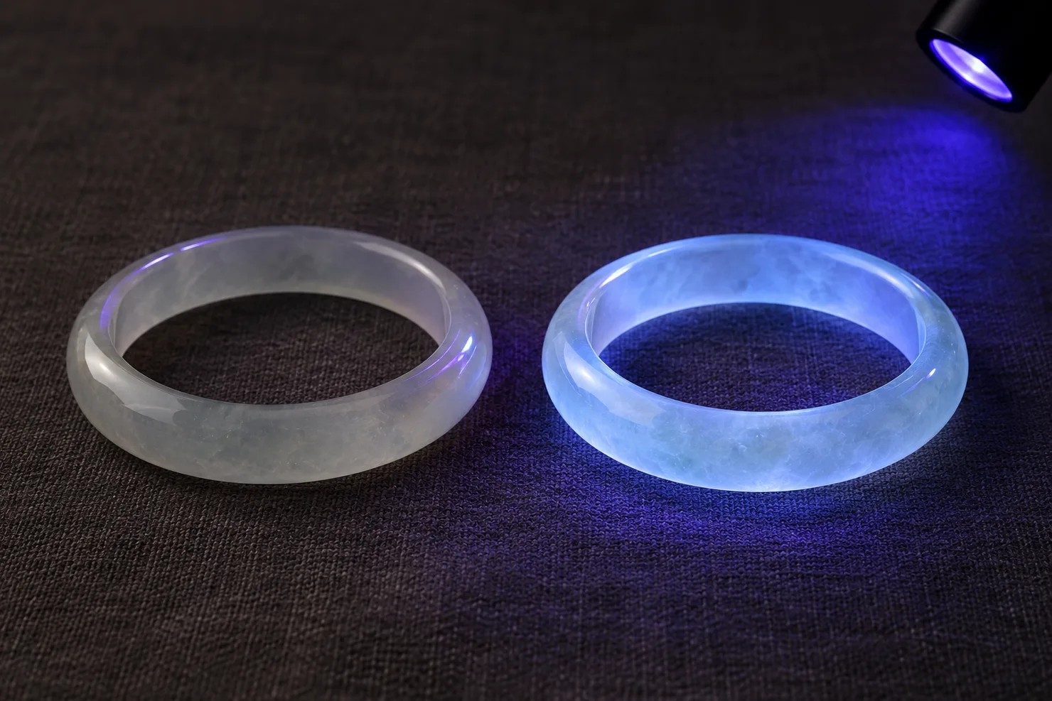 Two pale jadeite bangles under a small handheld UV lamp in a dim room: the left shows no glow, the right a clear bluish-white glow