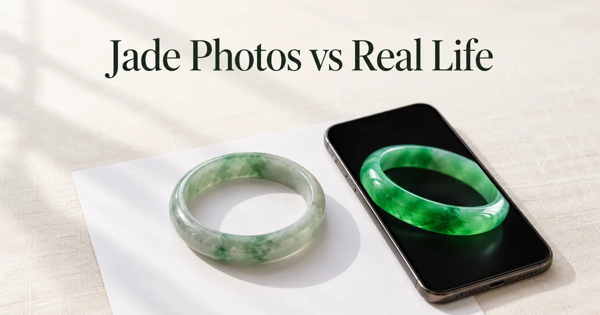 A smartphone on ivory linen showing a glowing green jadeite bangle on its screen, beside the same bangle lying on white paper in soft daylight, looking paler, with the title Jade Photos vs Real Life