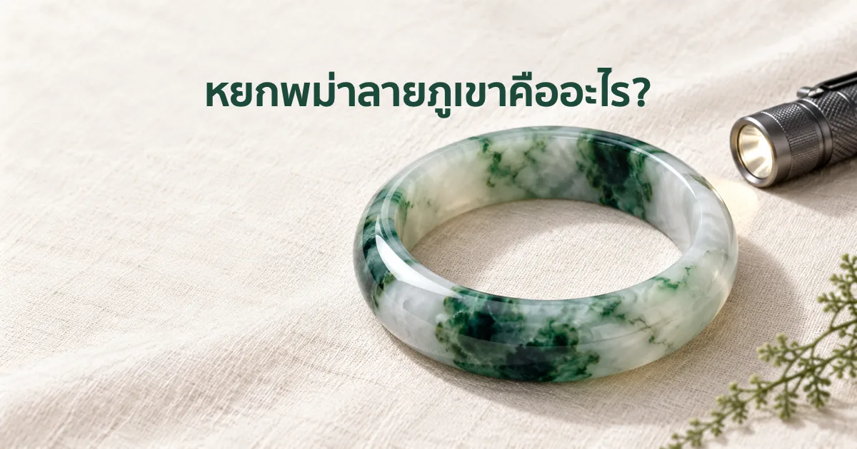 กำไลหยกพม่าพื้นขาวมีหย่อมและเส้นสีเขียวเข้มเหมือนภาพวาดทิวทัศน์หมึกจีน วางบนผ้าลินินสีงาช้างในแสงธรรมชาตินุ่มๆ ข้างไฟฉายเล็ก