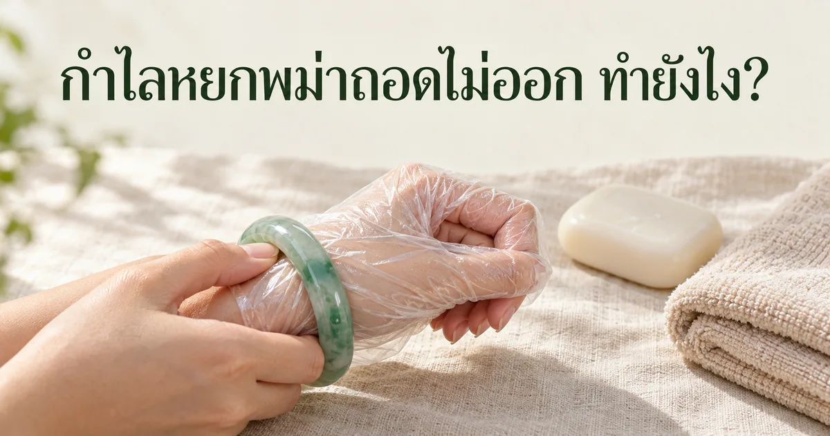 มือที่หุบนิ้วโป้งกำลังค่อยๆ ถอดกำไลหยกพม่าสีเขียวผ่านถุงพลาสติกบาง ข้างๆ มีก้อนสบู่และผ้าขนหนูพับบนผ้าลินินสีงาช้าง พร้อมหัวข้อ กำไลหยกพม่าถอดไม่ออก ทำยังไง?